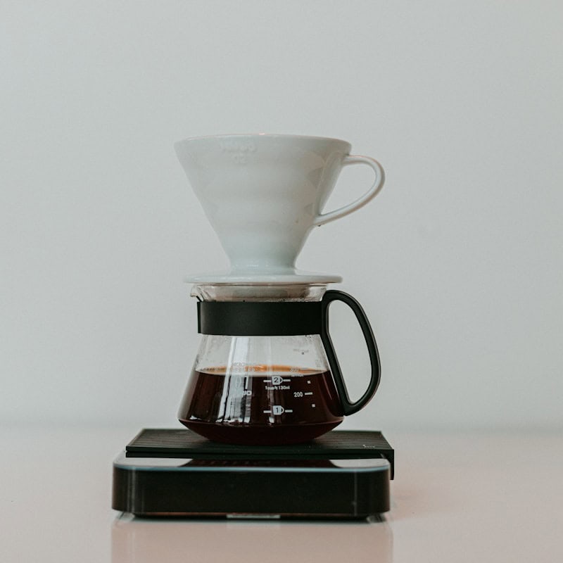 A Hario V60 pour-over coffee brewing set with a white ceramic dripper, glass server with brewed coffee, and a black digital scale - beann speciality coffee