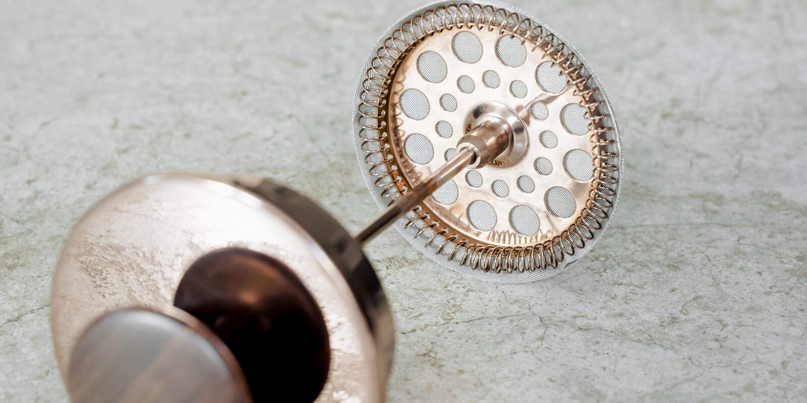 Close-up of a Beann Artisan Coffee french press coffee maker's rose gold metal filter and plunger mechanism -  beann speciality coffee