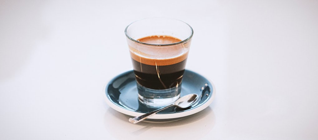 small glass of Beann artisan espresso with rich crema on a dark saucer - beann speciality coffee