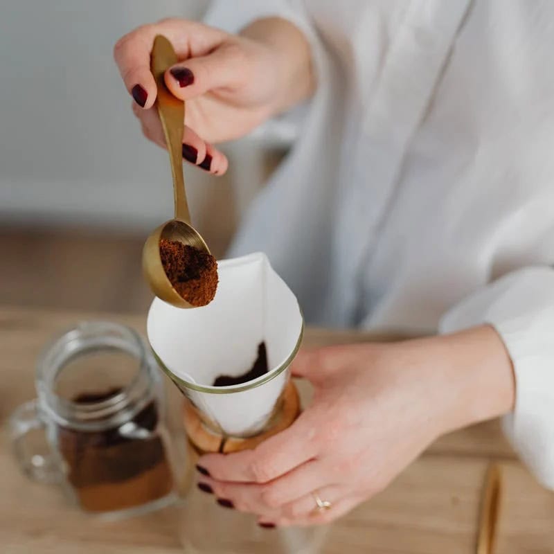 Hands pouring Beann artisan ground coffee into a white pour-over filter in a wooden stand - beann speciality coffee