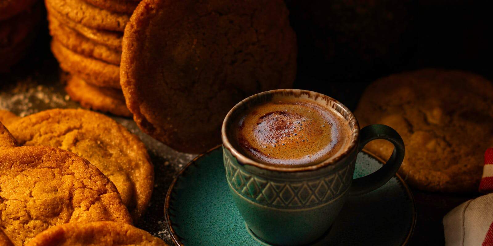 A small cup of coffee with crema on a teal saucer surrounded by ginger snap cookies - beann artisan coffee