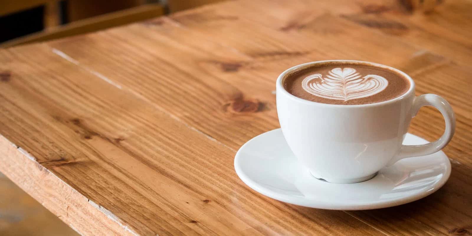 A white cup of Beann Artisan Coffee with latte art on a wooden table - beann speciality coffee