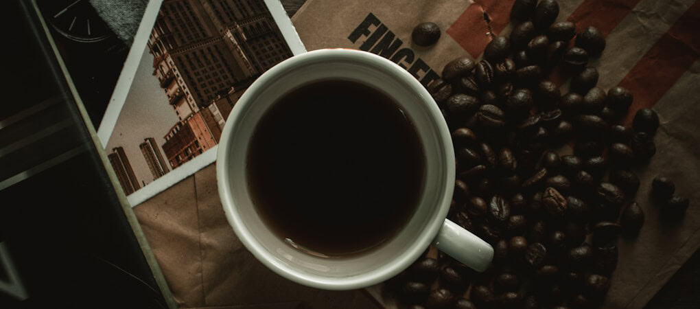 A cup of dark beann artisan coffee next to scattered coffee beans and a photo of city buildings - beann speciality coffee