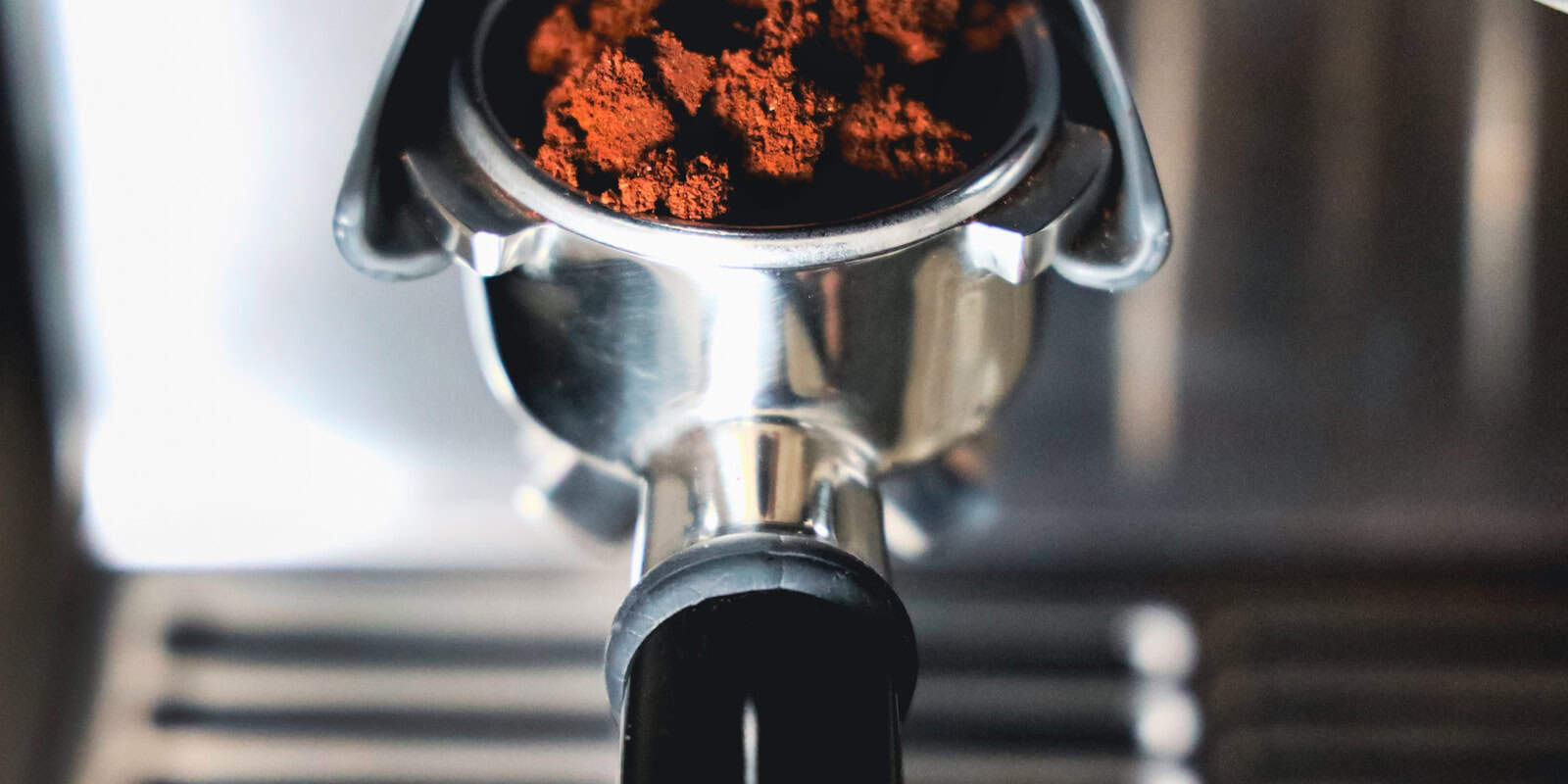 Close-up of a metal portafilter filled with dark, ground coffee beans, ready for brewing an artisan espresso - beann artisan coffee