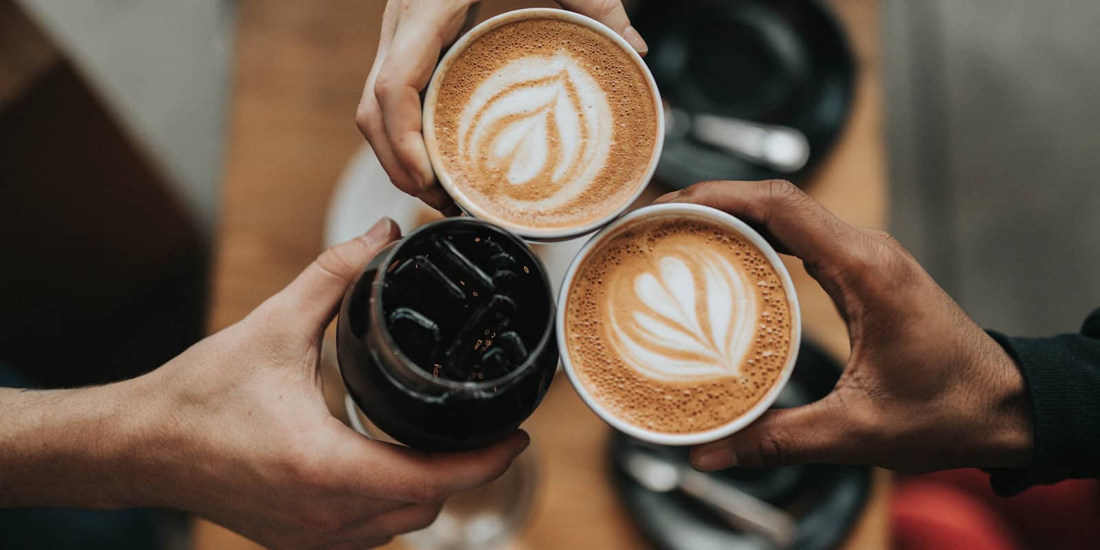 Three people toasting with two lattes featuring latte art and one iced coffee at Beann Artisan Coffee - beann speciality coffee