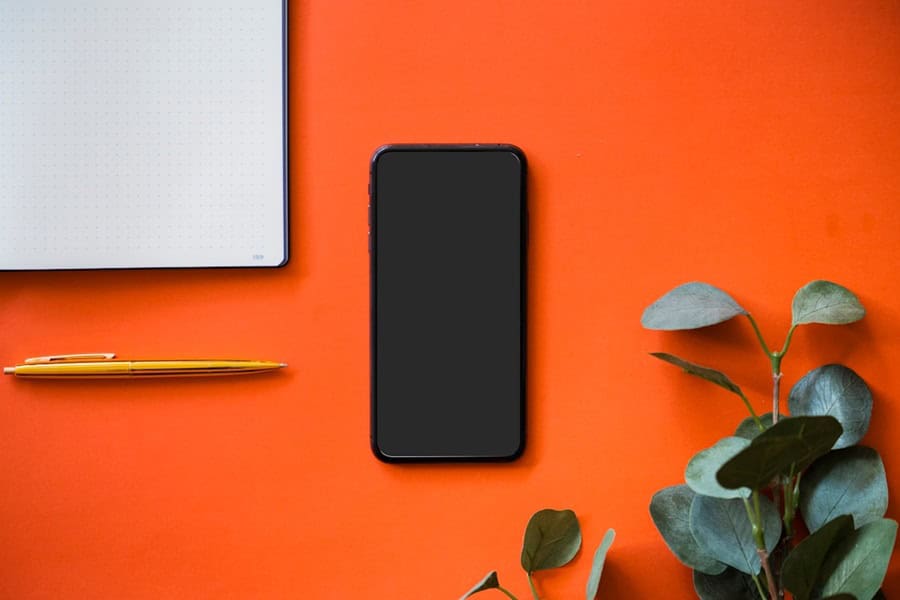 iphone pen and note pad on orange background - Top Digital Product Consultancy Services - photo unsplash | de Paula Consultants