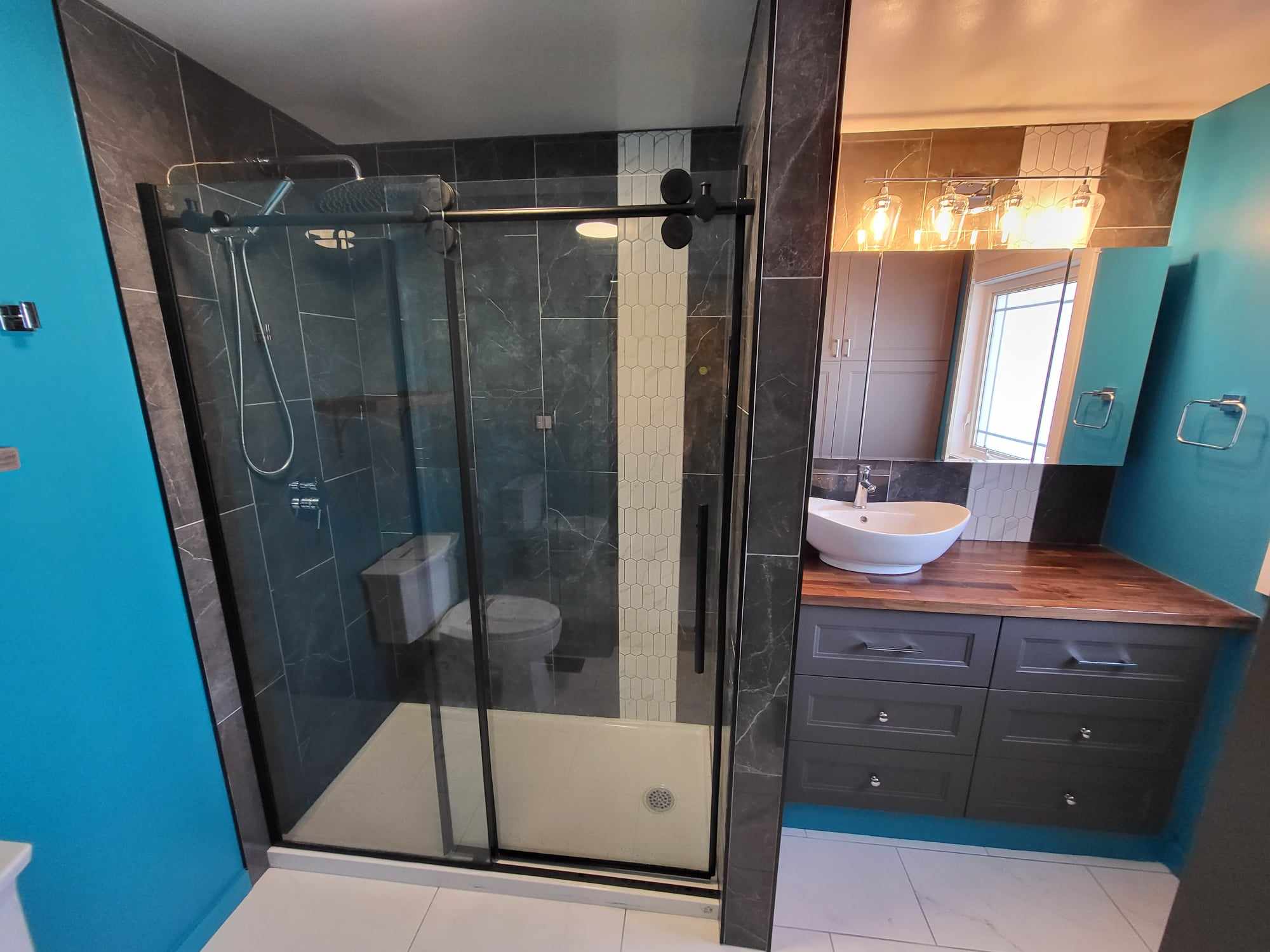 A elegant shower with a oak kitchen sink and beautiful dark tile job with a quartz mosaic accent border