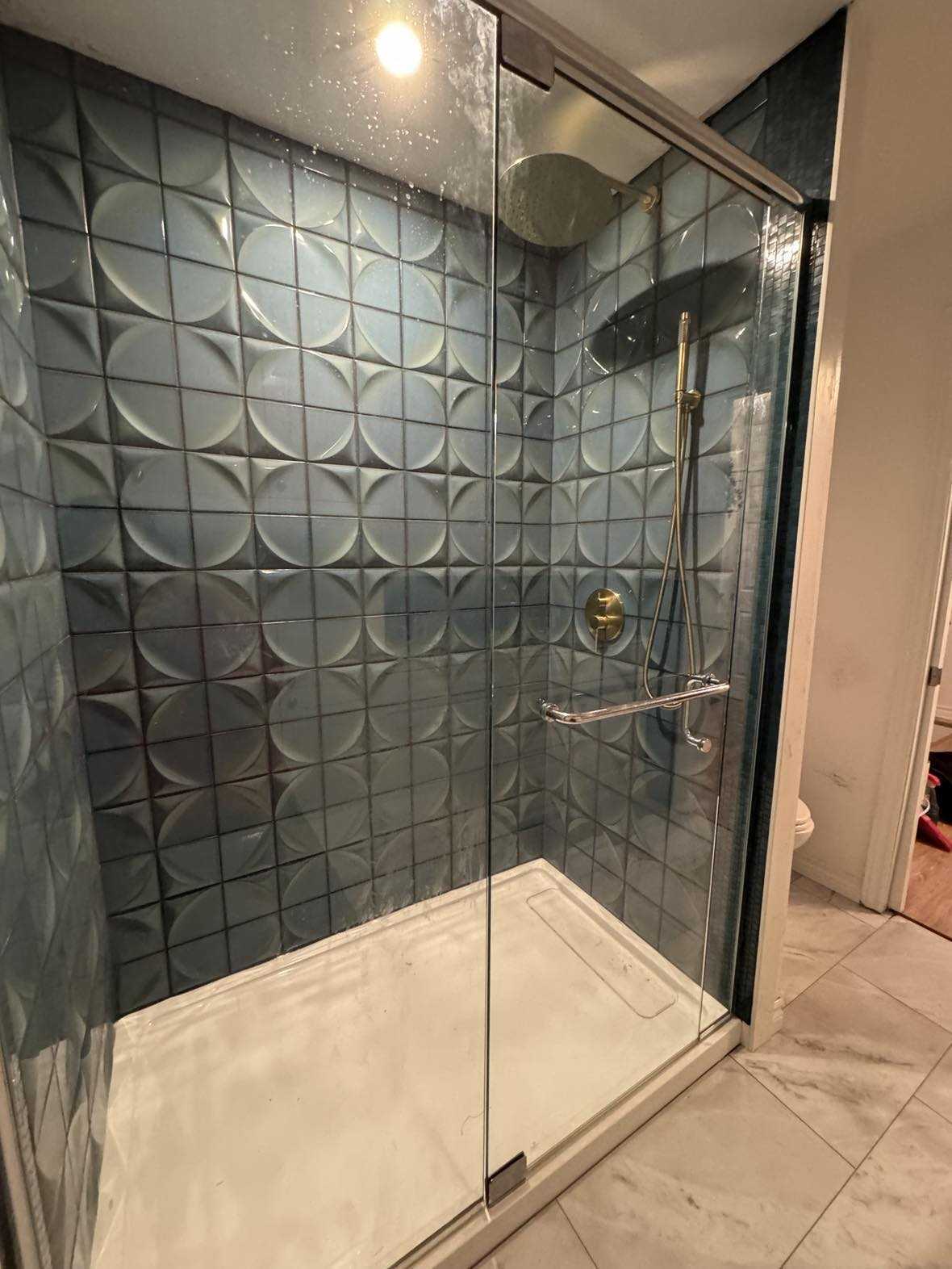 A phograph of a beautiful new shower stall with custom green gemotrically shaped porcelaine tiles