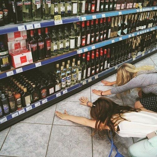 Deux personnes allongées devant un rayon d'alcool en magasin, capturant une scène humoristique ou décalée