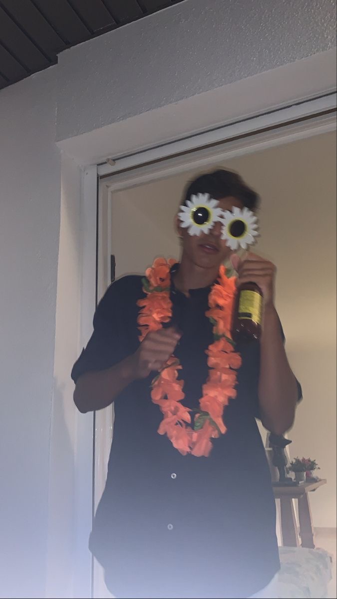 Personne portant des lunettes blanches et un collier de fleurs orange, posant dans une ambiance festive