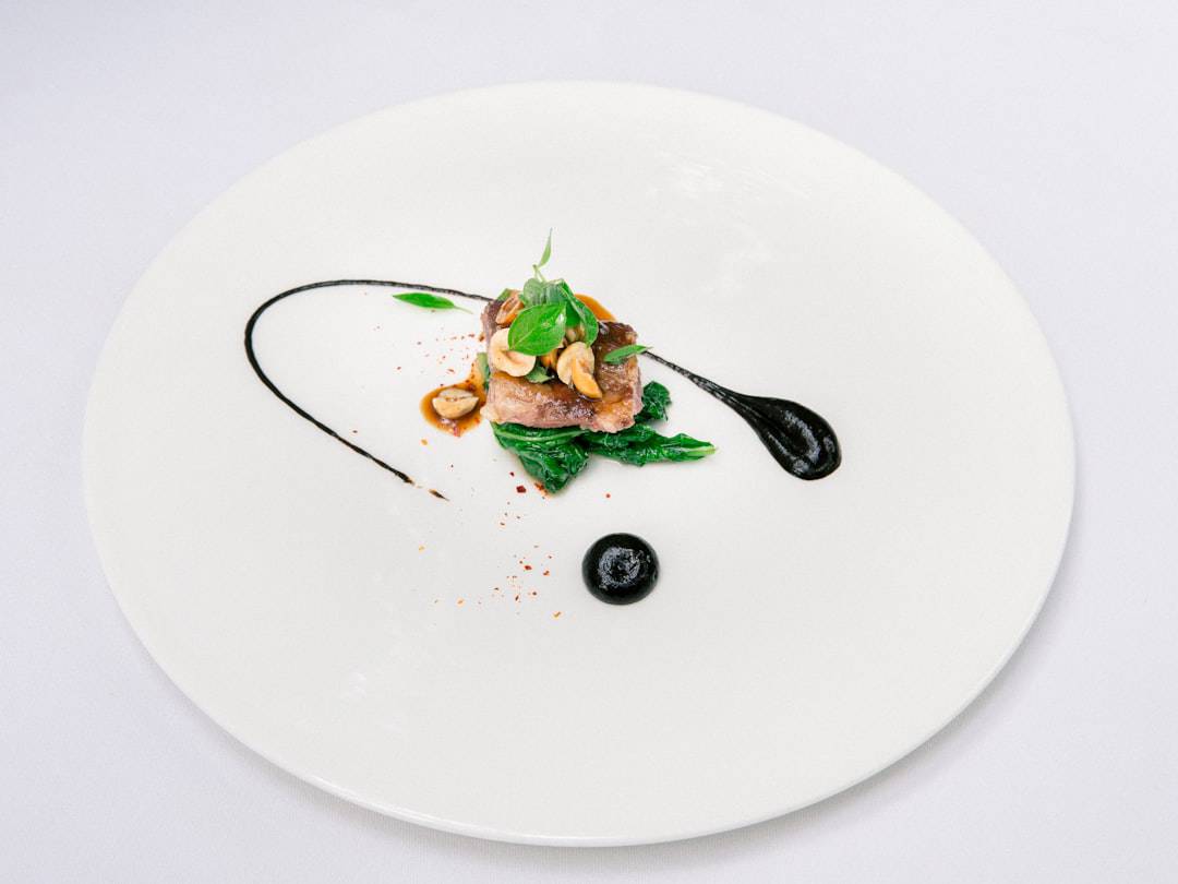 Cotswolds Village of Castle Combe, North Wiltshire, UK Gourmet dish featuring tender meat garnished with greens, nuts, and a drizzle of sauce on a white plate - Photo by Delightin Dee | Castle Combe England
