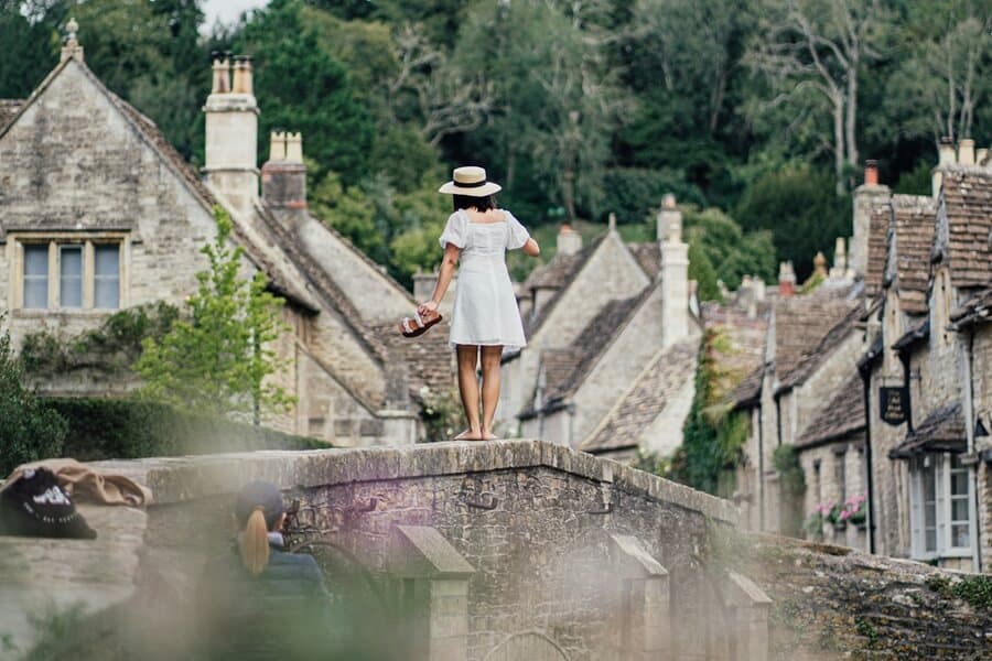 Woman Tourist on Bridge in Beautiful Castle Combe Village in the Cotswolds Wiltshire UK - Photo by Clement Proust Castle Combe England