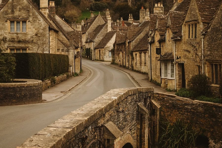 A winding road through the picturesque village of Castle Combe in the Cotswolds, England, lined with traditional honey-colored stone cottages | Castle Combe England