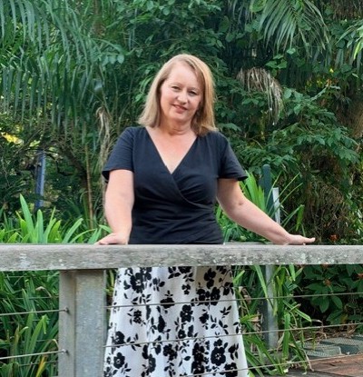 Sharon from Willow Connection standing beside a timber fence with tropical greenery behind her