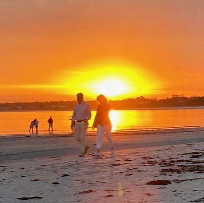 Two people walking along the shoreline at sunset, with golden light reflecting across calm water