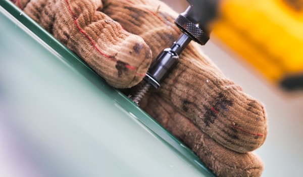 A pair of gloves holds a screw, demonstrating careful handling during a repair or assembly task.