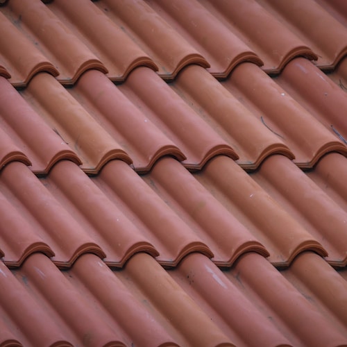 A close-up view of a red tile roof, showcasing the texture and color of the tiles against a clear sky.