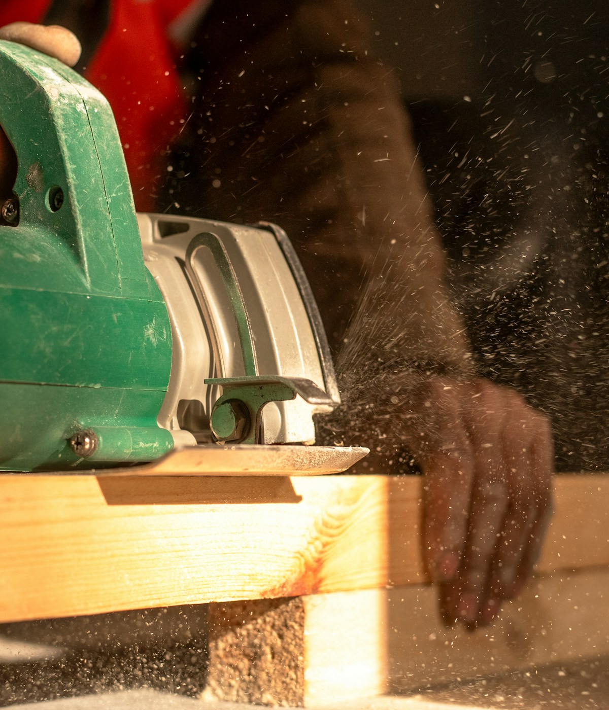 A person operating a circular saw to cut a piece of wood in a workshop setting.