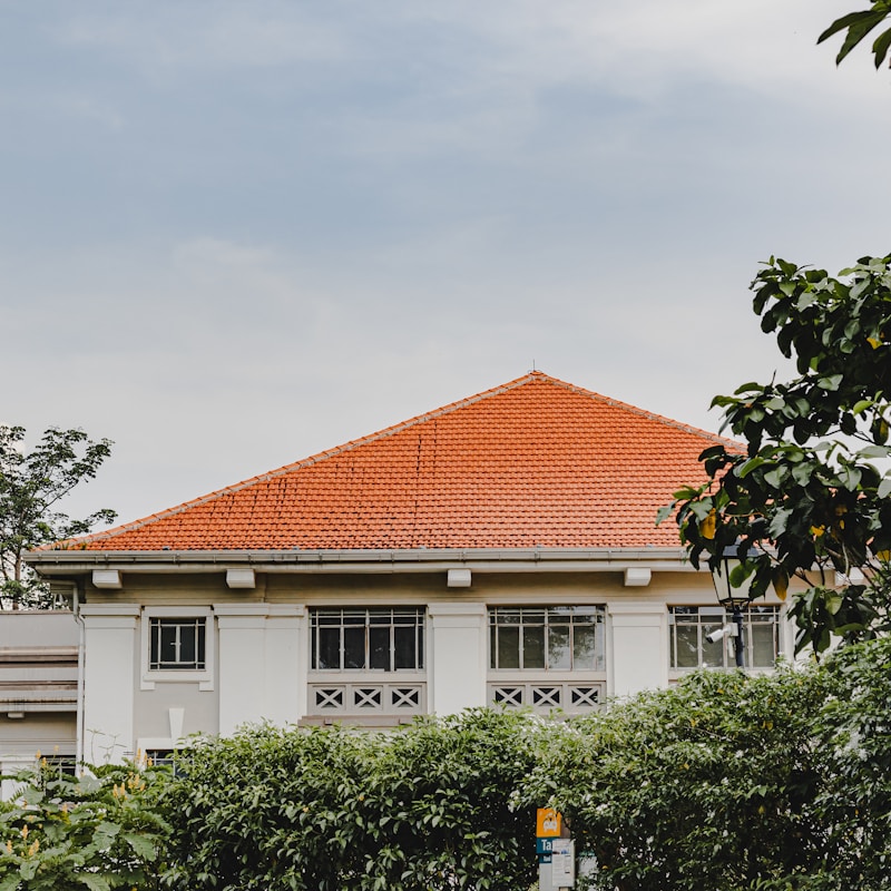 A building with a red roof surrounded by green trees in the foreground.