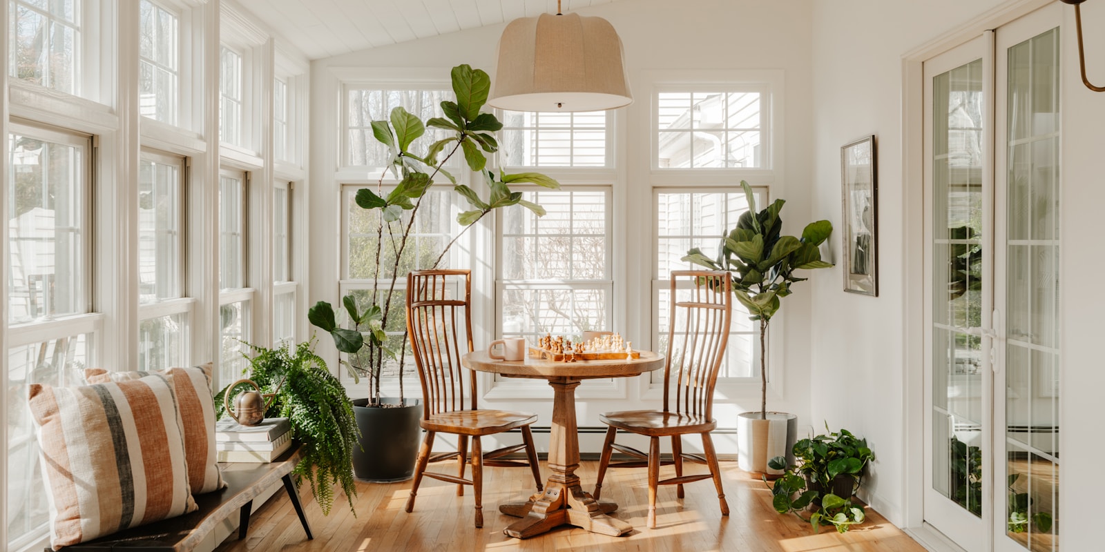 A bright sunroom featuring a table surrounded by chairs, inviting natural light and a cozy atmosphere.