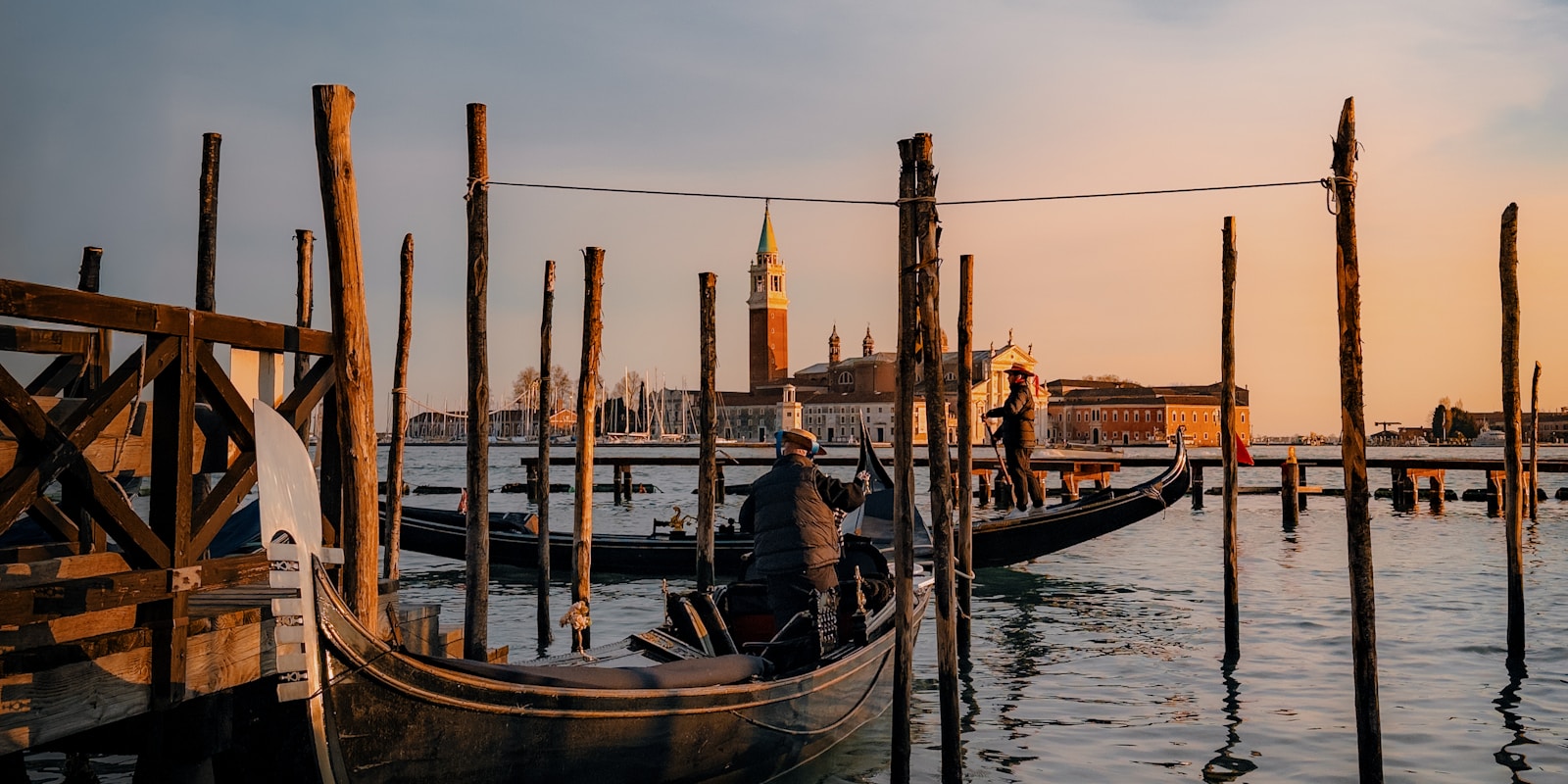 Gondolas glide through the canals of Venice at sunset, casting silhouettes against the vibrant sky.