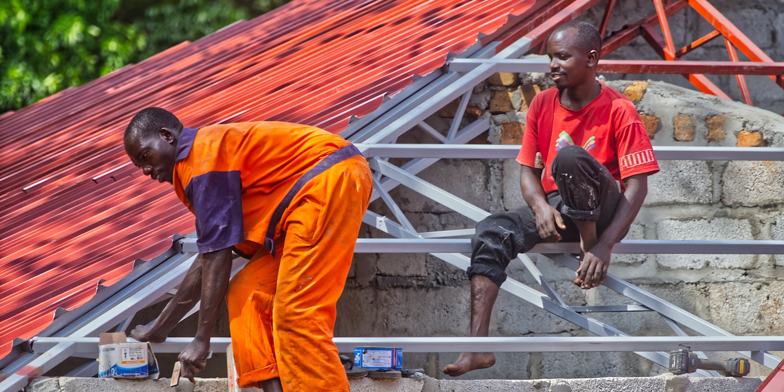 Two men in orange shirts working together on a roof, focused on their tasks and using safety equipment.
