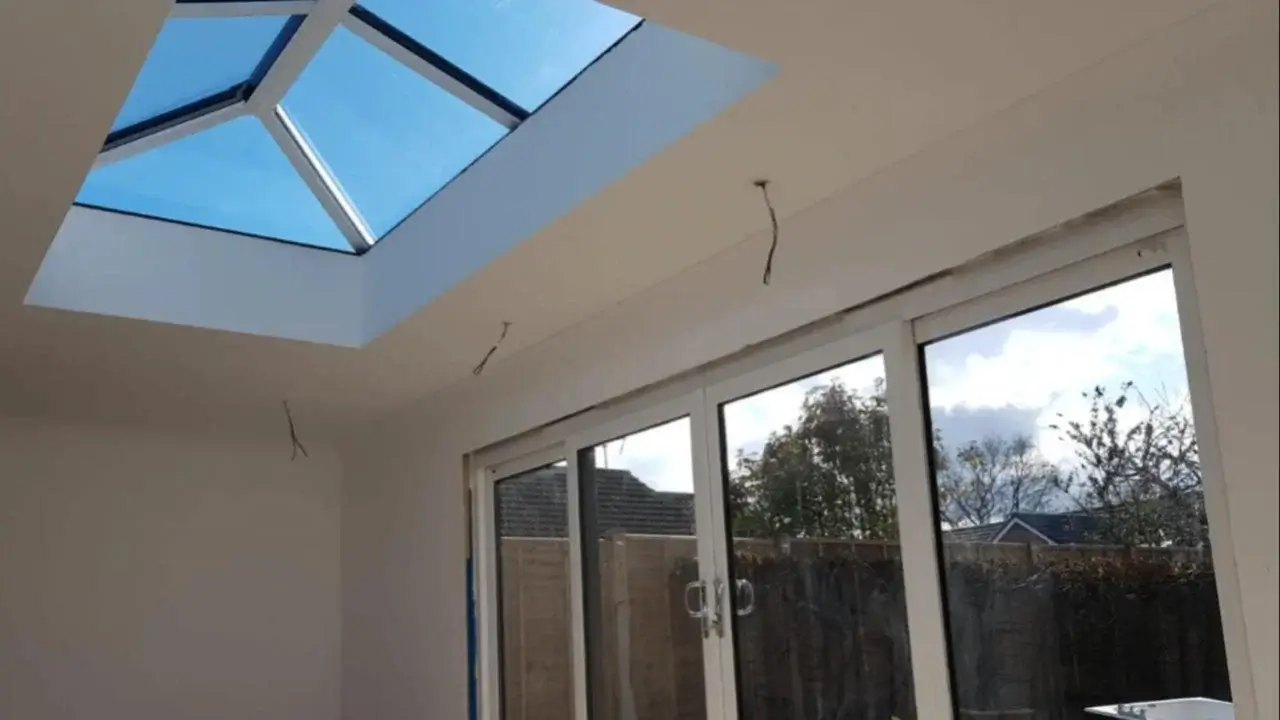 Bright interior of a conservatory conversion showing a large glass roof lantern design and white uPVC sliding patio doors by Norfolk Exterior Solutions.