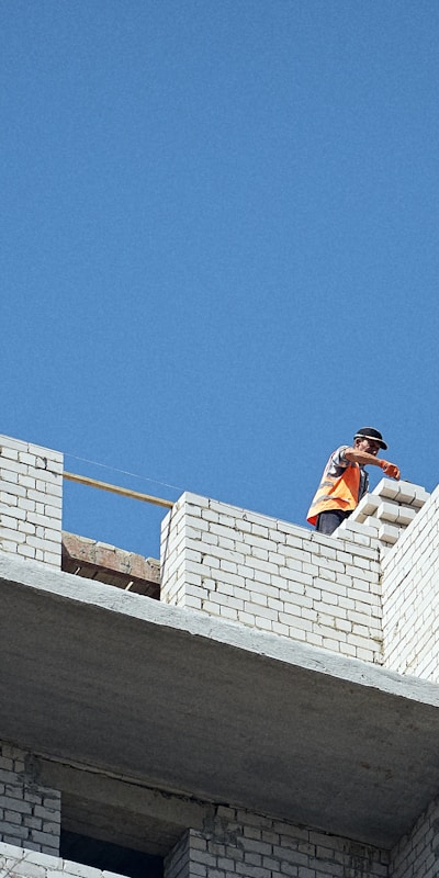 A man using a ladder to paint the exterior of a house in a residential neighborhood.