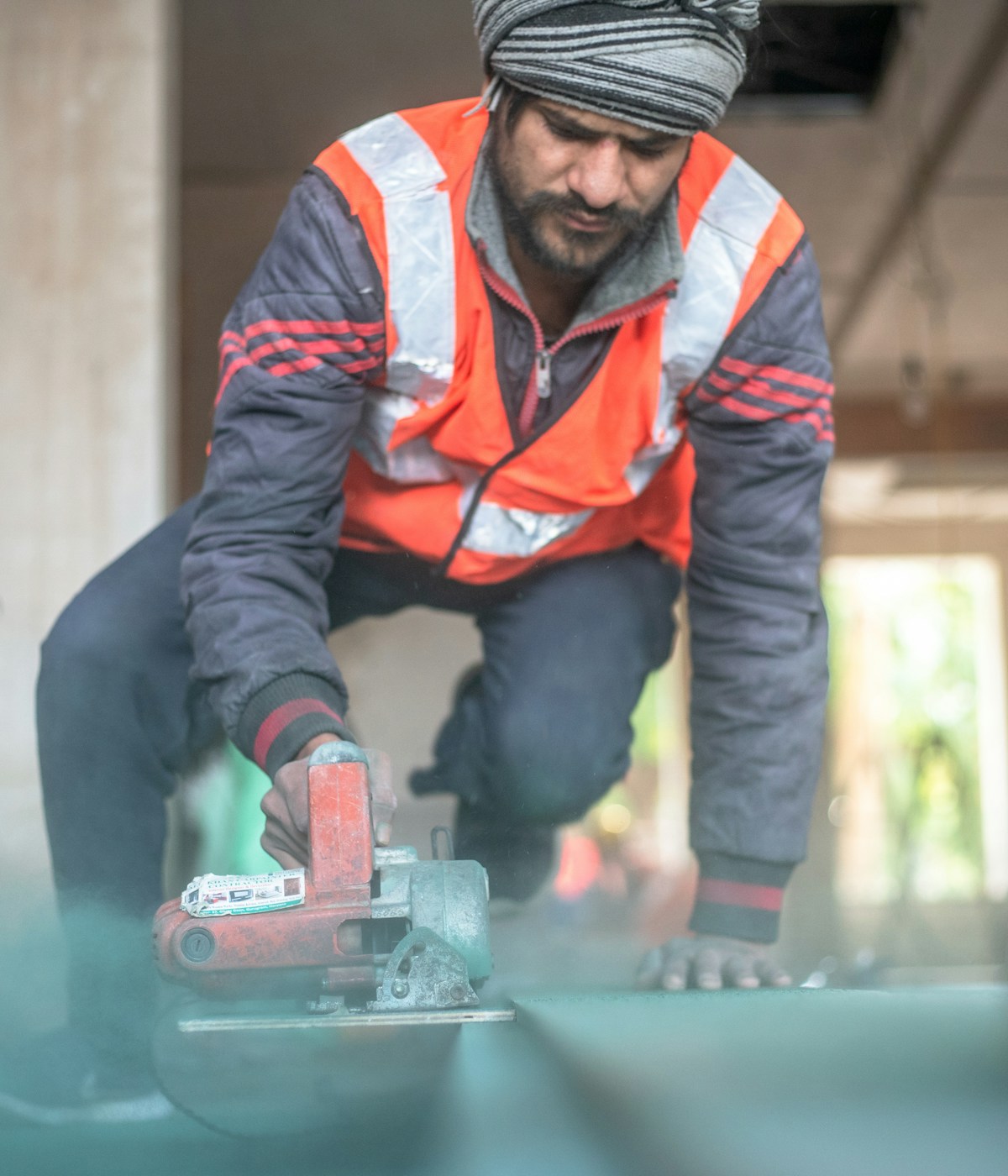 A man in an orange vest and hat operates a circular saw, focused on his woodworking task.