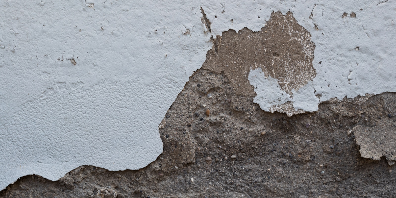 A close-up of a wall showing peeling paint, revealing layers of color and texture beneath the surface.