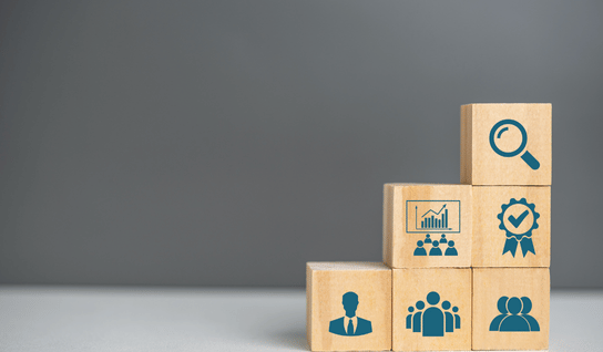 Wood table with porcelain mug, leather journal, brass pen, leather key ring, and a houseplant.