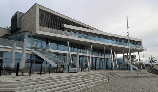 Desk with leather desk pad, walnut desk organizer, wireless keyboard and mouse, and porcelain mug.