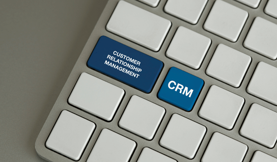 Desk with leather desk pad, walnut desk organizer, wireless keyboard and mouse, and porcelain mug.