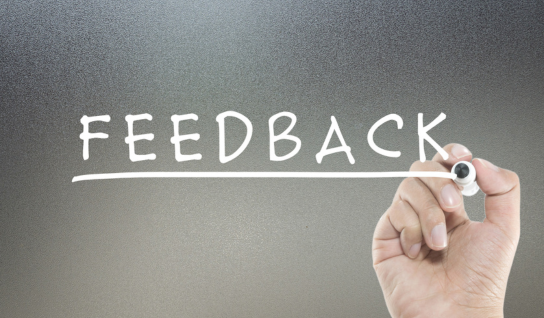Wood table with porcelain mug, leather journal, brass pen, leather key ring, and a houseplant.