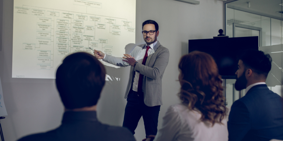 Wood table with porcelain mug, leather journal, brass pen, leather key ring, and a houseplant.