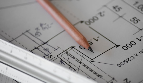 A pencil rests on top of a detailed blueprint, suggesting a design or planning process in progress.
