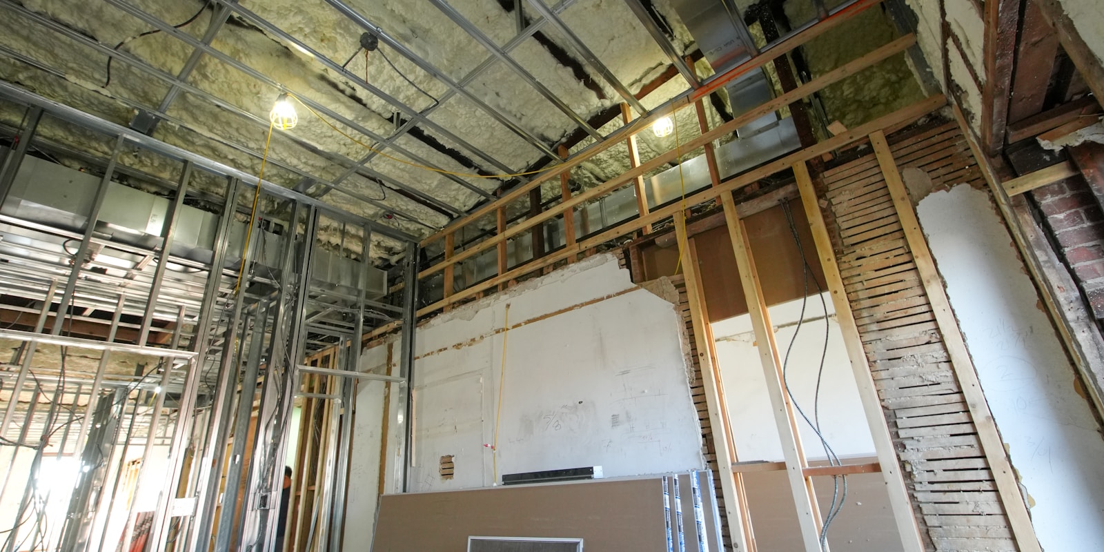 A room filled with construction materials, including wood and tools, alongside a bare wall awaiting finishing touches.