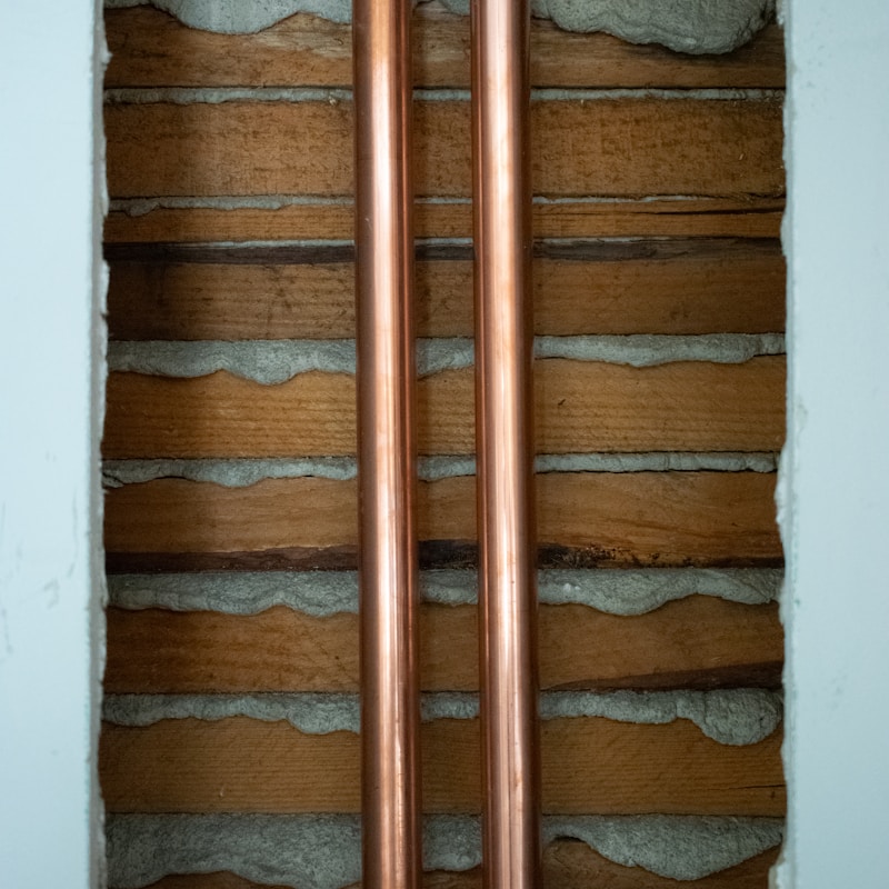 Two copper pipes are mounted on a wooden wall in a room, showcasing a blend of industrial and natural materials.