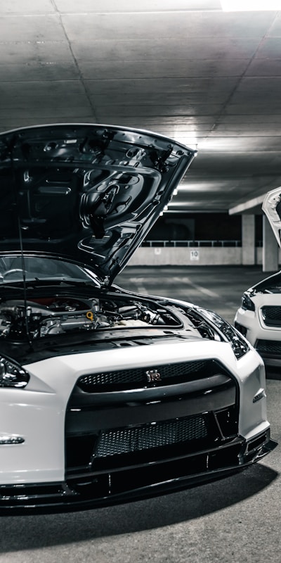Two white sports cars parked side by side in a dimly lit parking garage.