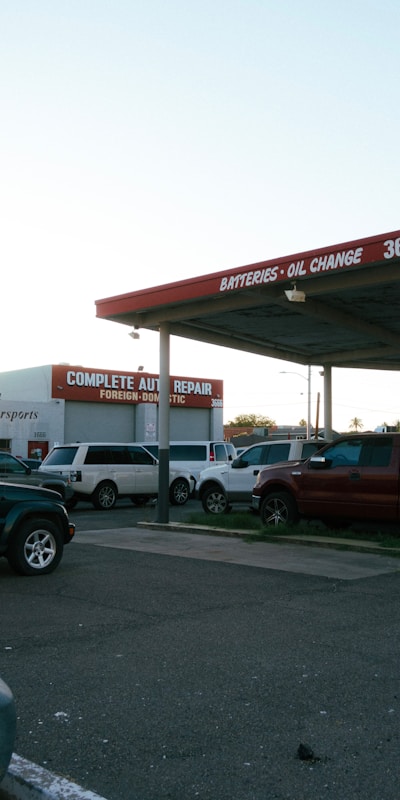 Outdoor view of an auto repair shop with signage for batteries and oil changes. Several parked vehicles are visible under a clear sky.