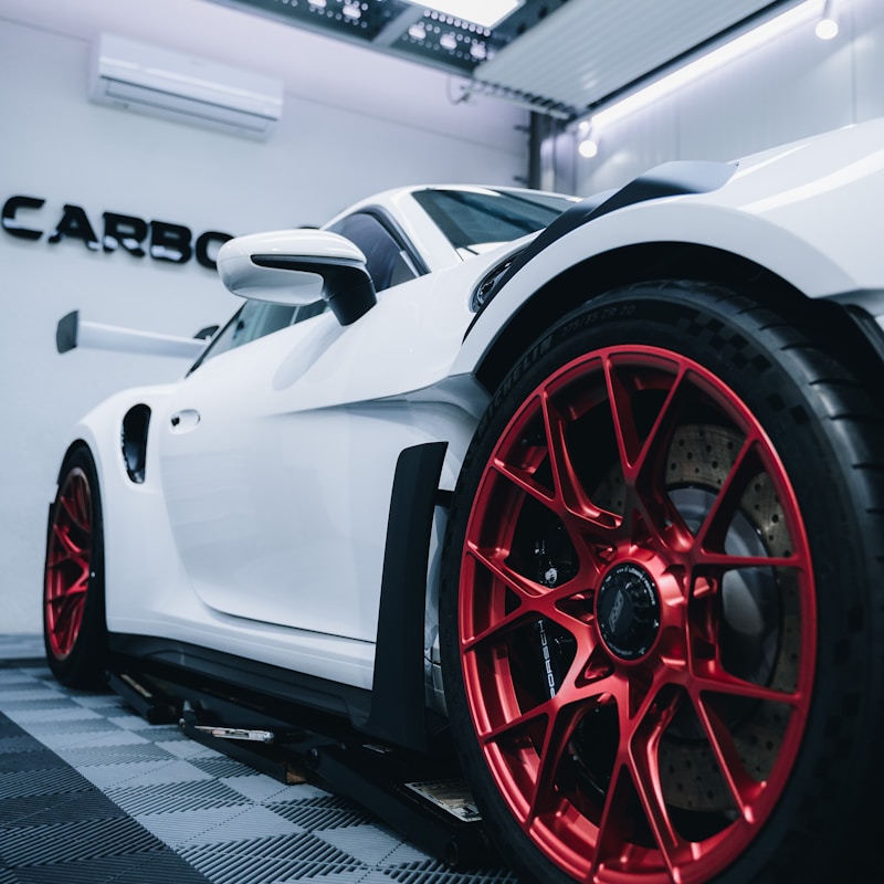 A sleek white sports car featuring striking red rims, parked against a neutral background.