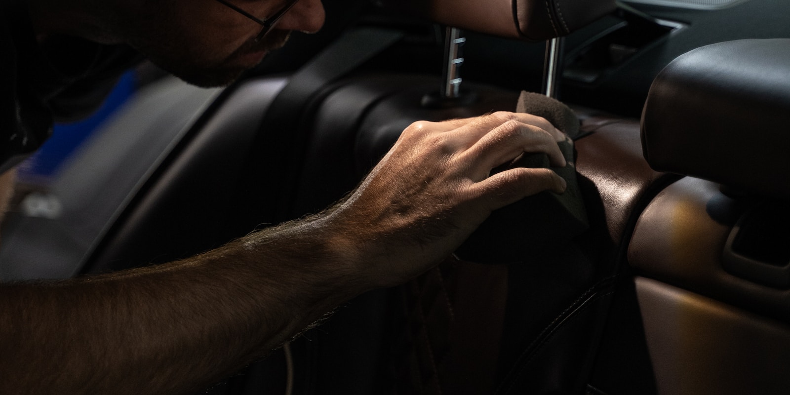 A man is repairing the seat of a car, focused on adjusting the upholstery and mechanisms.