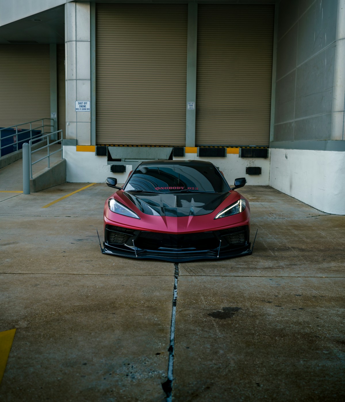 Sleek maroon sports car with black accents parked in an industrial setting. Its sharp lines and bold color convey a sense of power and style.