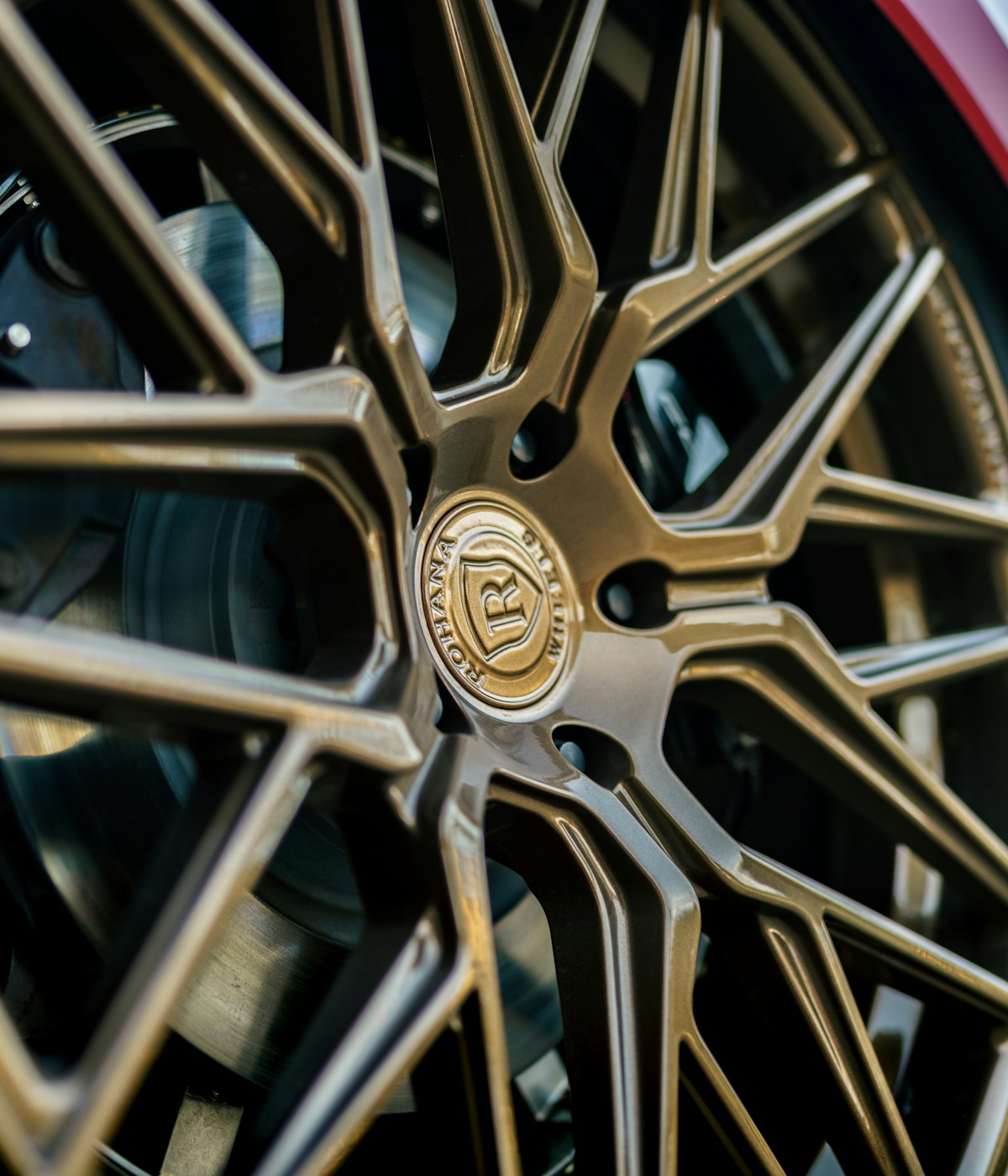 Close-up of a bronze alloy car wheel with intricate, star-shaped spokes. The center cap displays a logo, conveying elegance and precision engineering.