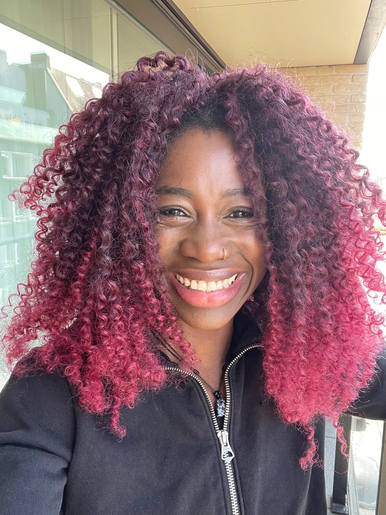 Sylvia smiling outdoors with curly pink-tinted hair