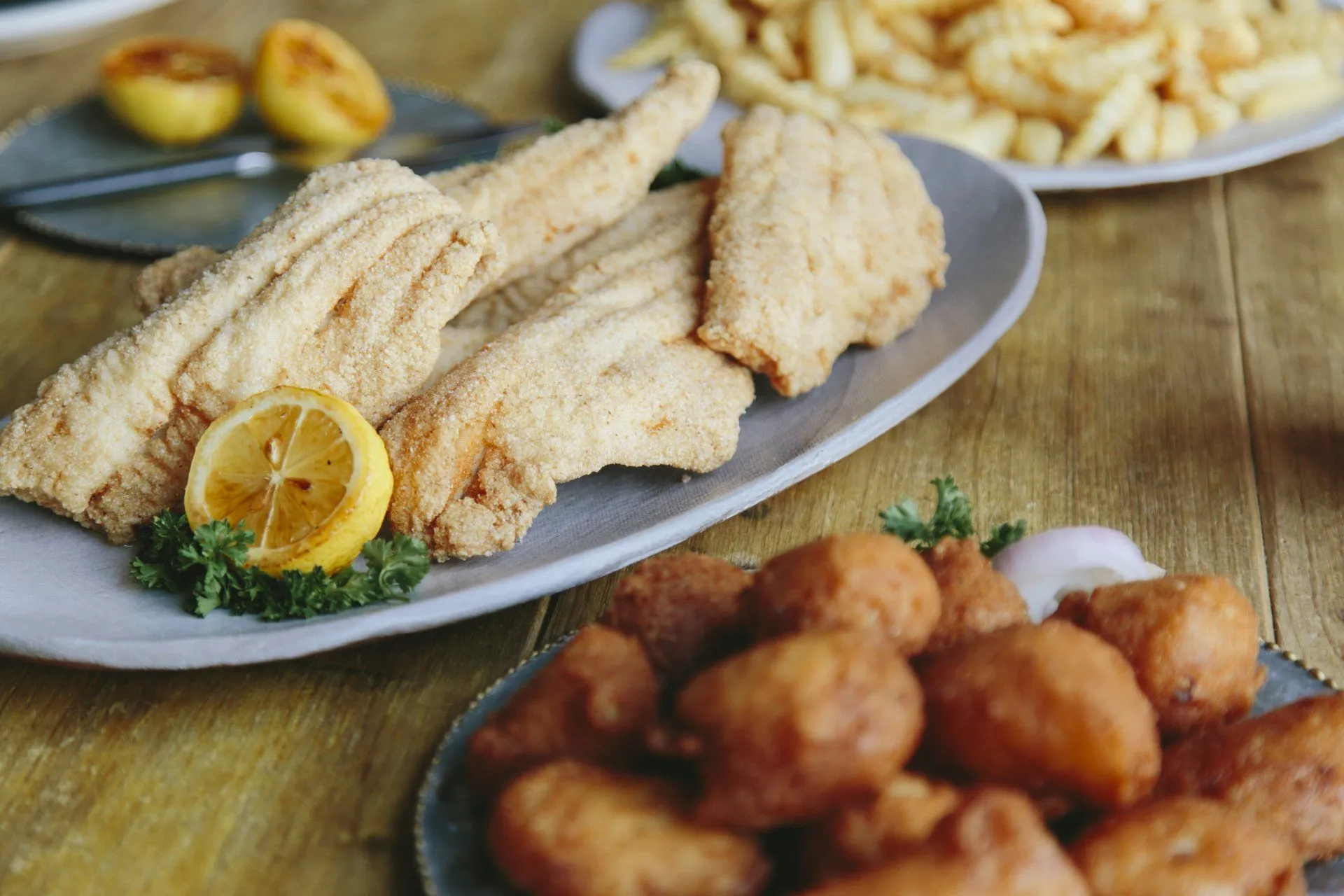 Plate of golden hand-breaded fried catfish served with lemon, fries and hushpuppies