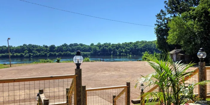 Open lawn with a wooden fence and lantern posts overlooking the river on a sunny day
