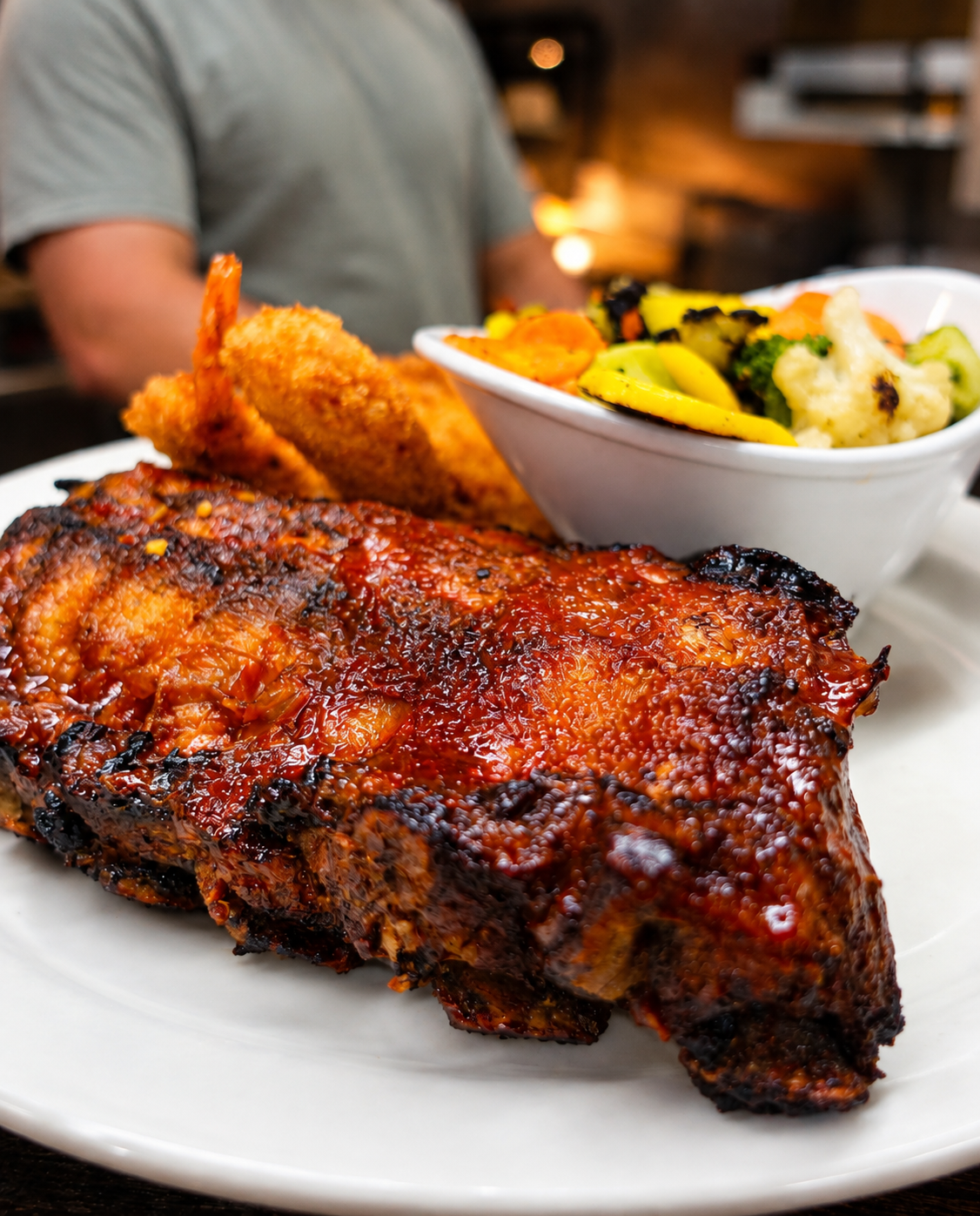 Plate of glazed barbecue ribs with fried shrimp and a side of vegetables
