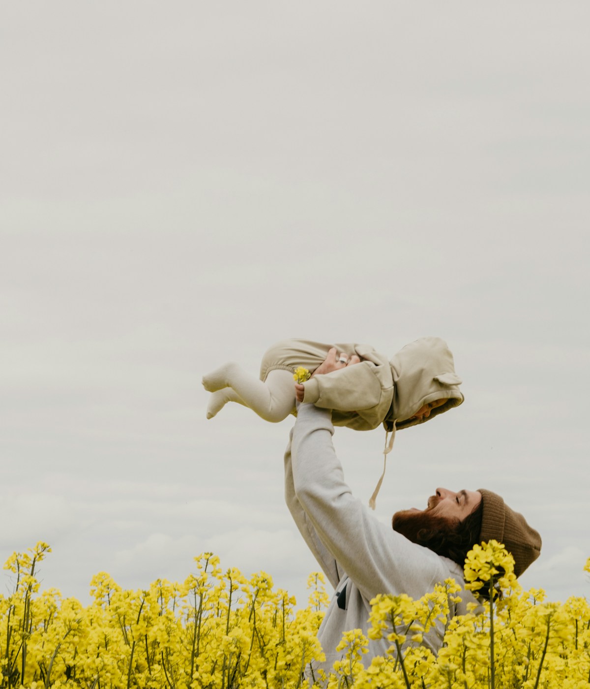 Vater hält sein Baby hoch über den Kopf auf einer Rapswiese