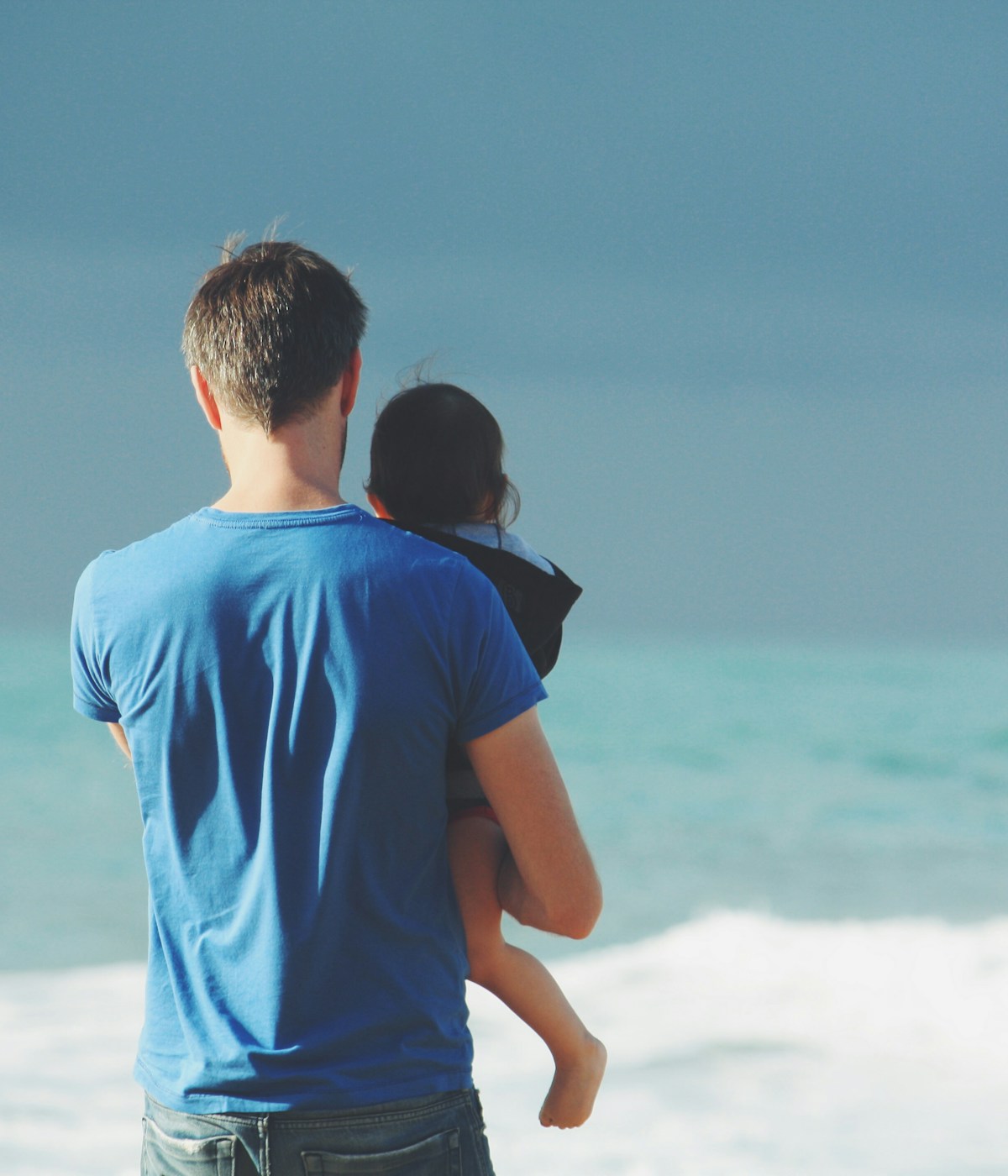 Vater hält Kind ruhig auf dem Arm und betrachtet das Meer